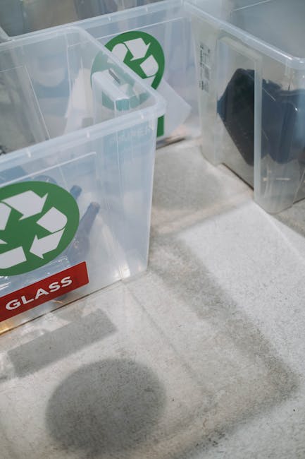 Close-up image of transparent plastic recycling bins placed on a light-colored carpeted floor inside a property. The bins are marked with green recycling symbols on the side and have labels indicating