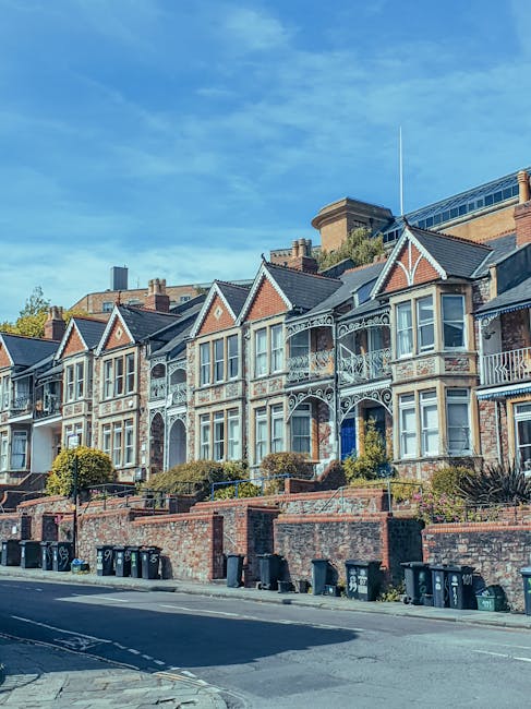 A wide view of a densely populated residential area featuring a hillside of closely spaced houses with tiled roofs, in various shades of brown, grey, and white. In the foreground, leafless tree branch